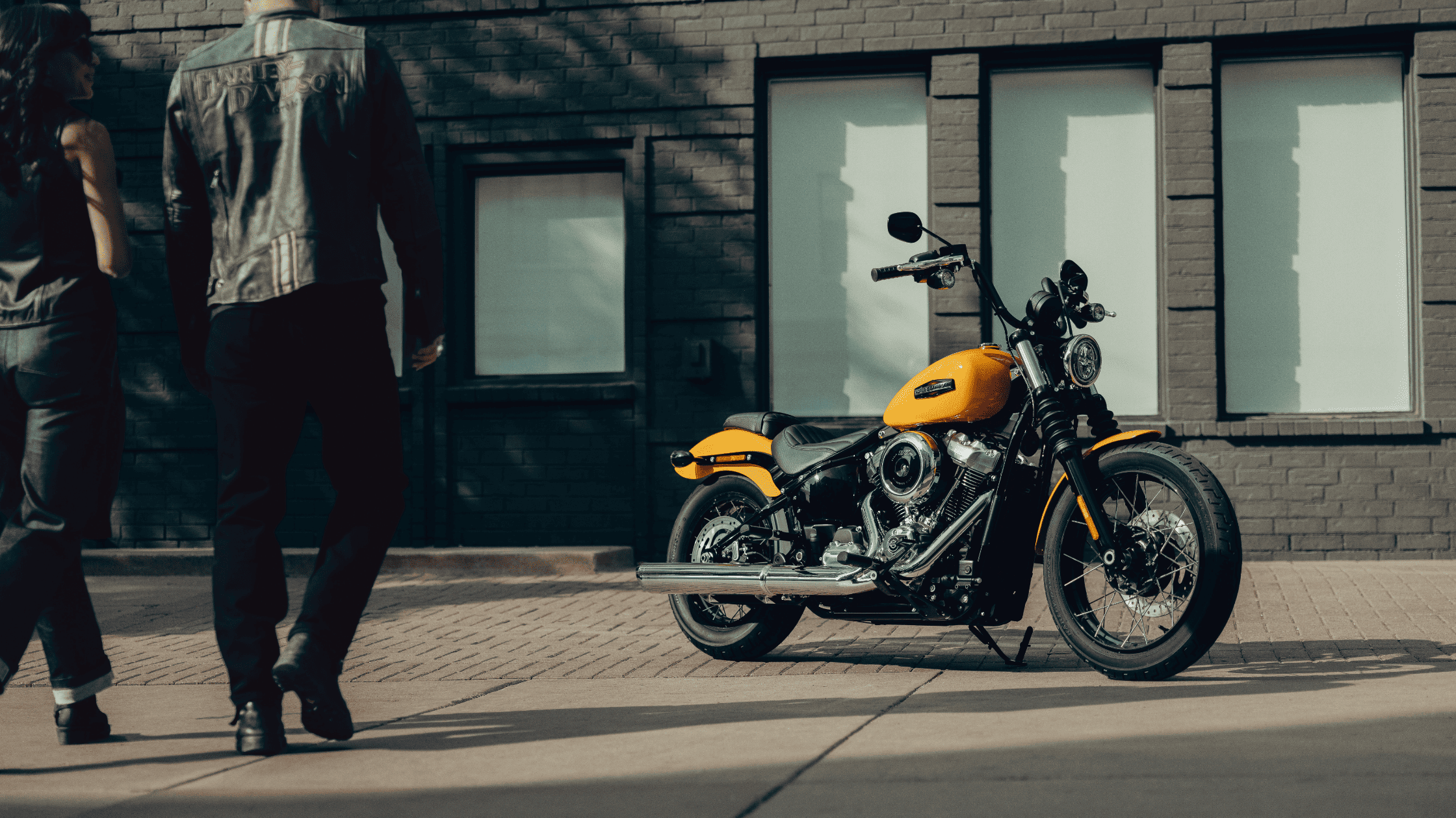 The 2025 Harley-Davidson Street Bob parked outside a modern brick building in Lincoln, NE, as two riders approach.